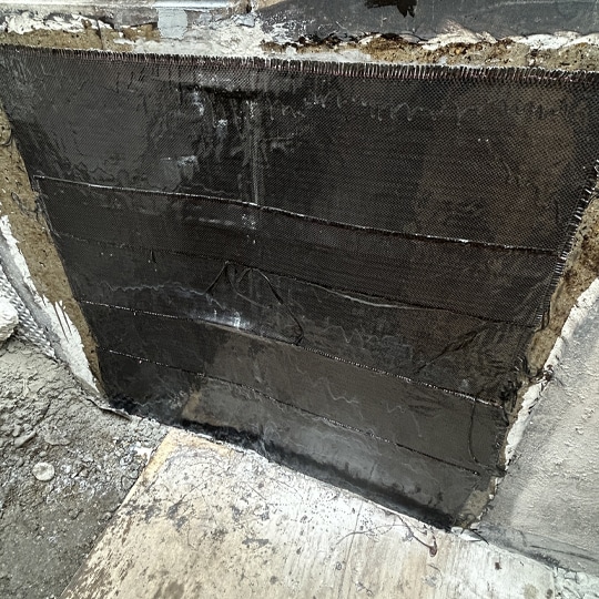 A concrete wall featuring a textured surface coated in black paint, creating a stark and modern aesthetic